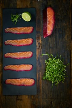 Sliced salmon fillet, sauteed with beetroot juice over black slate surface. Top view