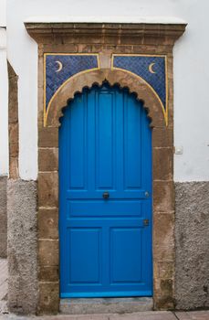 Bright blue color of the gate. Frame with an arch made of stone. Two moons decoration. White wall.