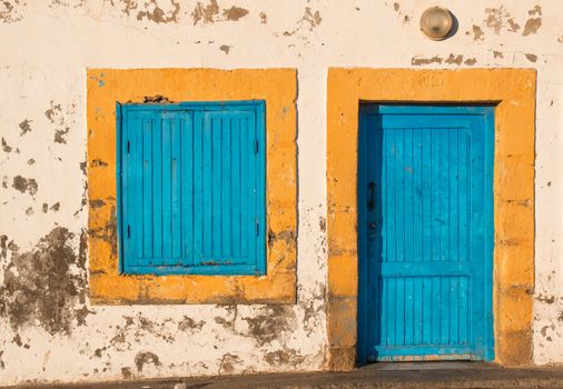 Old facade of a house with yellow framed window and door, both blue. Lamp above the door.