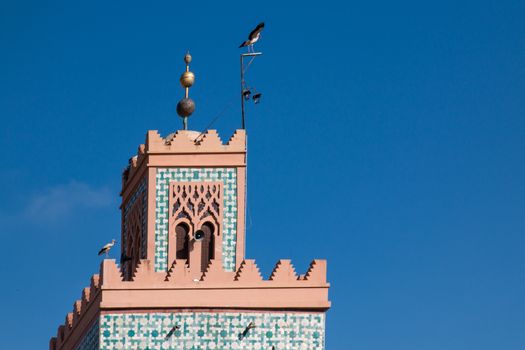 Detail of the minaret - tower of a mosque. Two birds - storks. Bright blue sky.