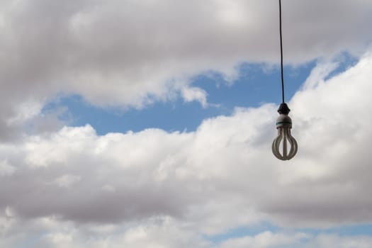 Light bulb hanging on a cable. Cloudy sky in the background.