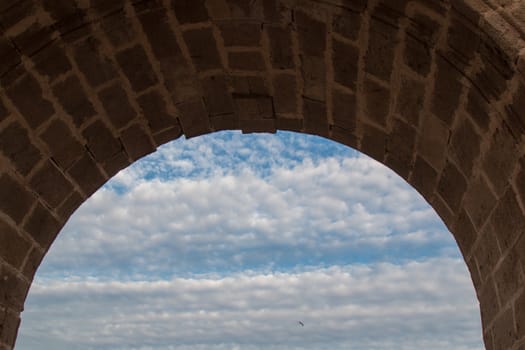 Detail view on an arc made of stone bricks. Very cloudy sky in the background. One bird.