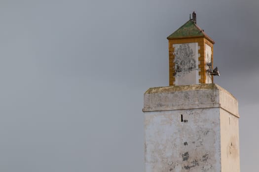 Minaret of an old mosque in Morocco. Yellow details and green roof. Cloudy rainy sky in the background.