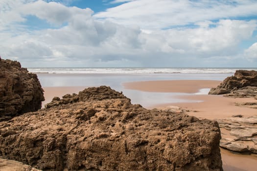 Cloudy day on a sandy beach of Atlantic Ocean in Morocco. Big rocks in the foreground.