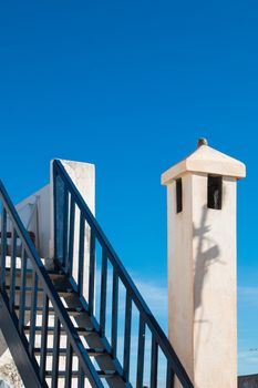 On the roof of the house. Blue painted stairway and a chimney. Bright blue morning sky.