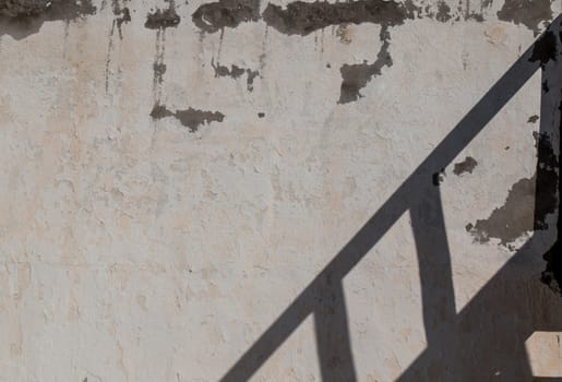 Old wall enlightened by sun, shadow of a stairs handle.