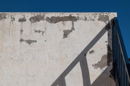 Old wall in the exterior, shadow of a handle of the stairs. Bright blue sky.