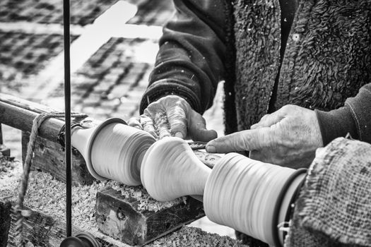 An artisan carves a piece of wood using an old manual lathe.