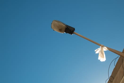 Streetlamp with a piece of plastic, enlightened by sun. Bright blue sky.