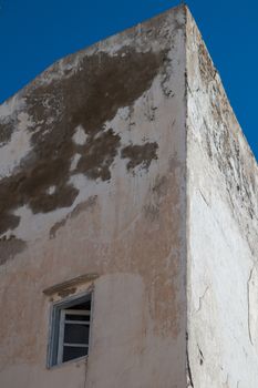 Corner of an old house in Essaouira, Morocco. Old damaged facade. Opened blue framed window. Bright blue sky.