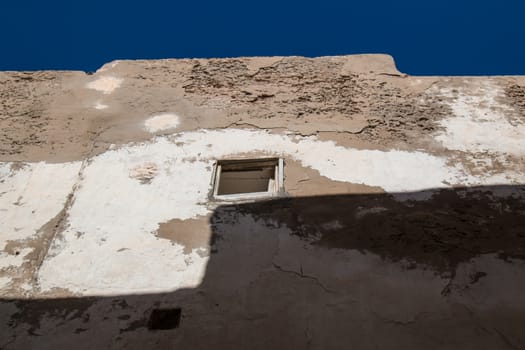 Old and destroyed wall of a house with a window without glass. Bright blue sky.