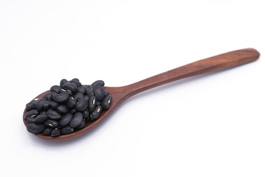 Black beans in wooden spoon isolated on white background