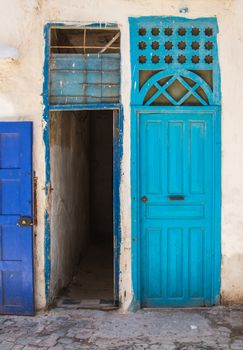 Wooden closed door painted blue and another door opened. Facade of an old house.