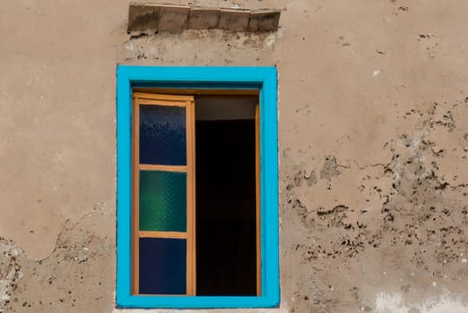 Brown facade of a old house with an opened window with a bright blue frame.