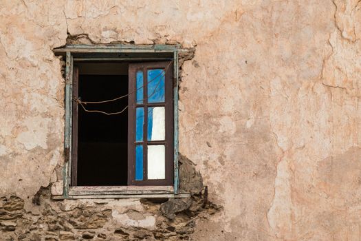 Brown facade of a old house with an opened window with a bright blue reflection of a sky and white reflection of a building.