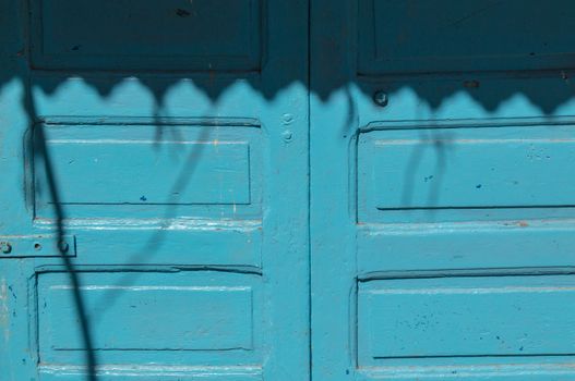 Old blue wooden gate, partly enlightened by sunshine, partly in a shadow created by a blind.