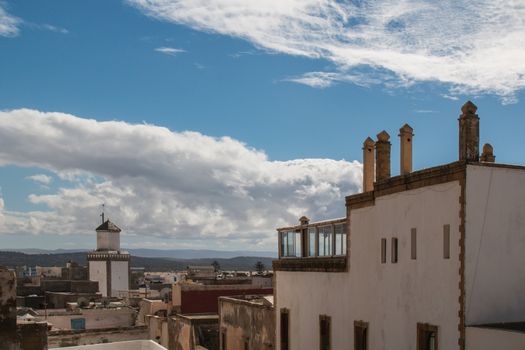 View from a roof on the downtown of Essaouira, Morocco. Residential houses, mosque and mountains in the background. Cloudy sky.