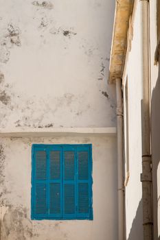 View on the corner of old houses in the city Essaouira in Morocco. Old wall, enlightened by sunshine and a window with blue shutter.