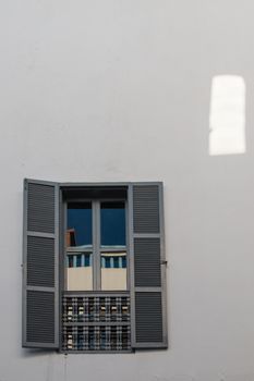 Closed window with a reflection. Opened shutters. White wall.