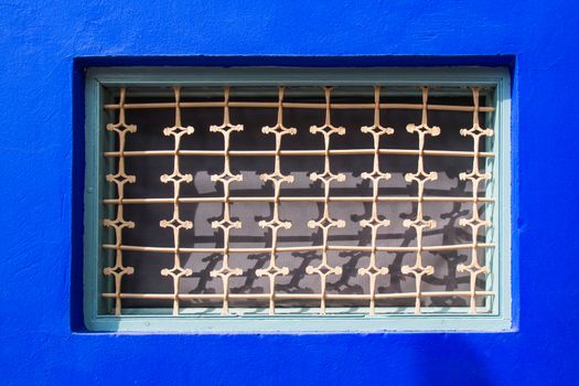 Vibrant blue color of the building facade, framing a window with a grid with traditional arabian pattern.