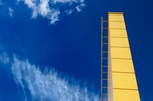 Contrast combination of bright yellow color of a pile and stairs with a blue sky with white clouds.