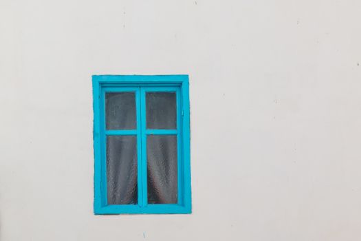 White wall with a window with a blue frame. Behind the structured glass are visible white curtains.
