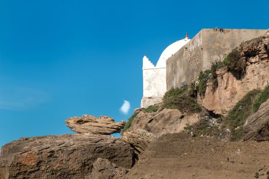 Part of an old small mosque, hidden between the rocks. Bright blue sky with just one white cloud.