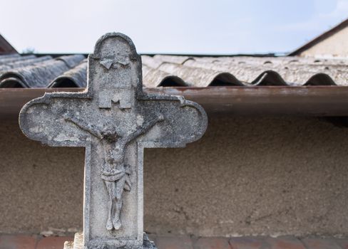 Old cross on the cemetery with a Jesus statue. Part of a structured roof in the background.