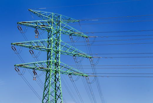 Green painted electricity tower detail with a blue sky in the background.