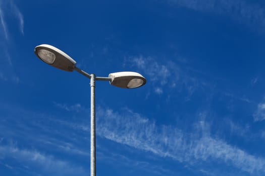 Detail of a double street lamp with a background of a blue sky with some light white clouds.