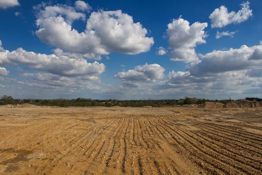 Land prepared for building. Patter in the soil. Small forest in the background. Blue sky with many white clouds.