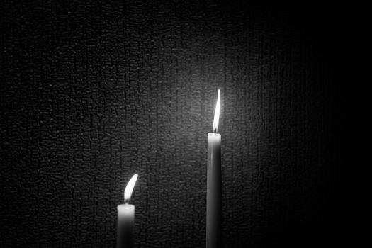 A black and white shot of two candles at different height shot against a textured wall.
