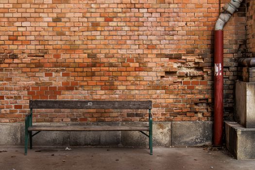 Various tones of orange color of the bricks wall. Old wooden bench.