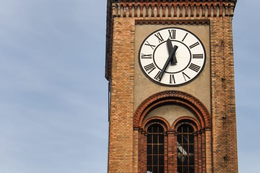 Tower with bricks details. Contrast clock with a white dial. Twenty five to twelve. Blue sky in the background.