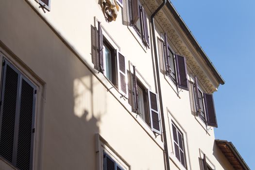 Detail of the roman residential house with enlightened shutters of the windows. Bright blue sky in the background.