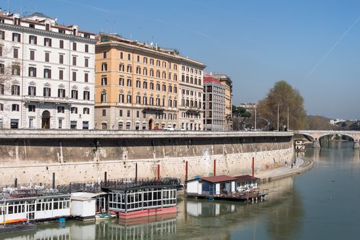 Embankment of Tiber with residential houses. Boats on the river. Bridge in the background. Summer blue sky.