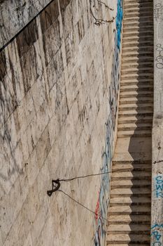 Long staircase from the Tiber riverbank to the promenade. Made of stone. High wall on the left side with graffiti.