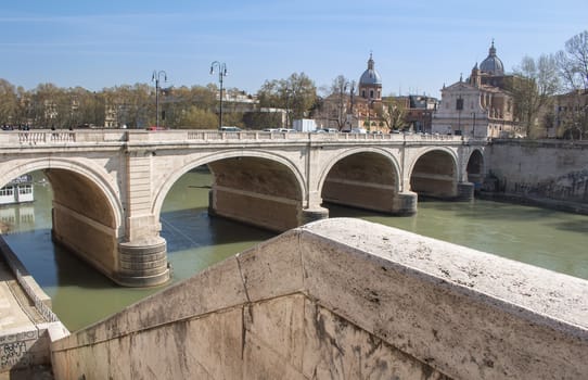 Part of Rome close to the Castle. Old bridge over the Tiber River. Buildings of the old city in the background. Blue sky with few white clouds.