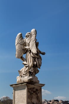 Another point of view on a statue of an angel at the bridge in italian Rome. Blue sky with some clouds in the background.