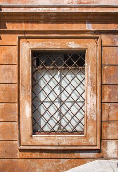 Window of an old building in the city of Rome, Italy. Window is protected by diagonal grating. Terracotta color of the house, typical for houses in Rome.
