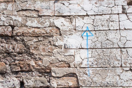 Old damaged wall with a blue painted arrow pointing up.