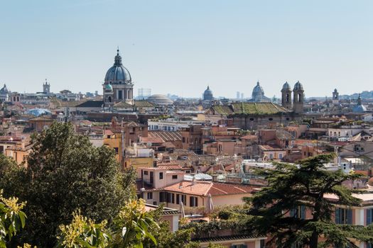View on the italian capital from a hill. Dome of a church and roofs of the residential houses. Trees in the foreground.