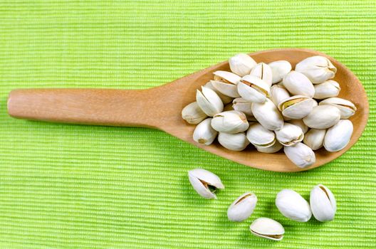 pistachio nuts in a wooden spoon on green background