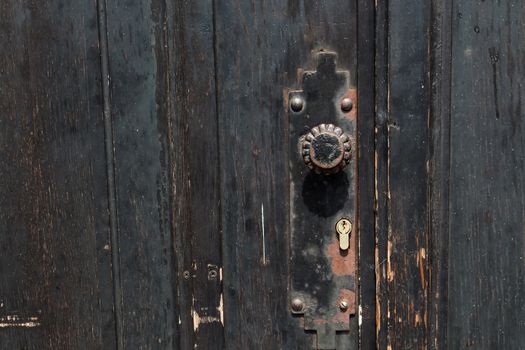 Dark painted wooden door. Detail of a handle and a lock.