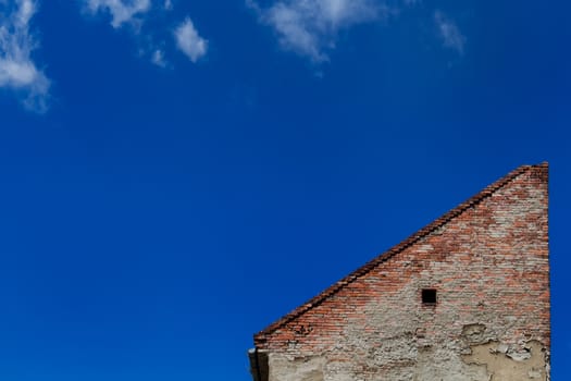 Lonely house. Wall made of bricks creates a triangle. Bright blue sky with several small clouds.