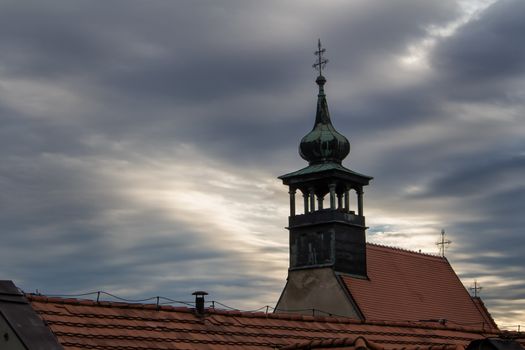 Church of St. Nicolas in Bratislava, Slovakia. Early cloudy rainy morning. Heavy dark clouds broken by a sunshine. Roof in the foreground.