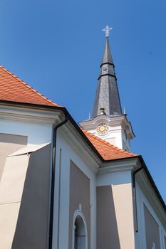 Details of the architecture of a small catholic church. Tower with a cross. Bright blue sky. Tomasikovo, Slovakia.