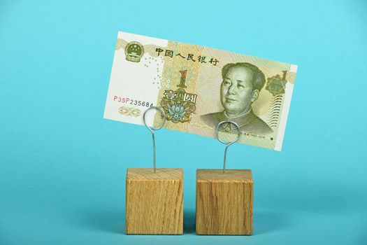 China economy crisis, decline of Chinese yuan illustrated, one yuan banknote at wooden metal holders over blue background