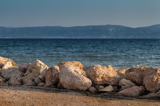 Coast of the second biggest island in Greece - Evia, place named Eretria. Line of a coastal stones, sea with small waves and mountains in the background.