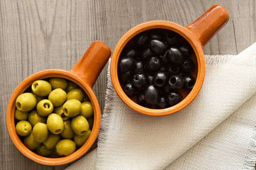 Two bowls of black and green olives, on old wooden Board.